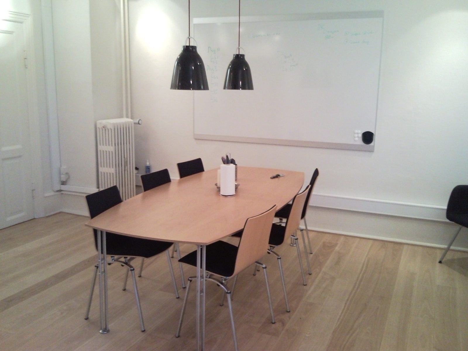 A meeting room in an old Copenhagen building, with a wooden table, black pendant lamps, a radiator and a large whiteboard with notes