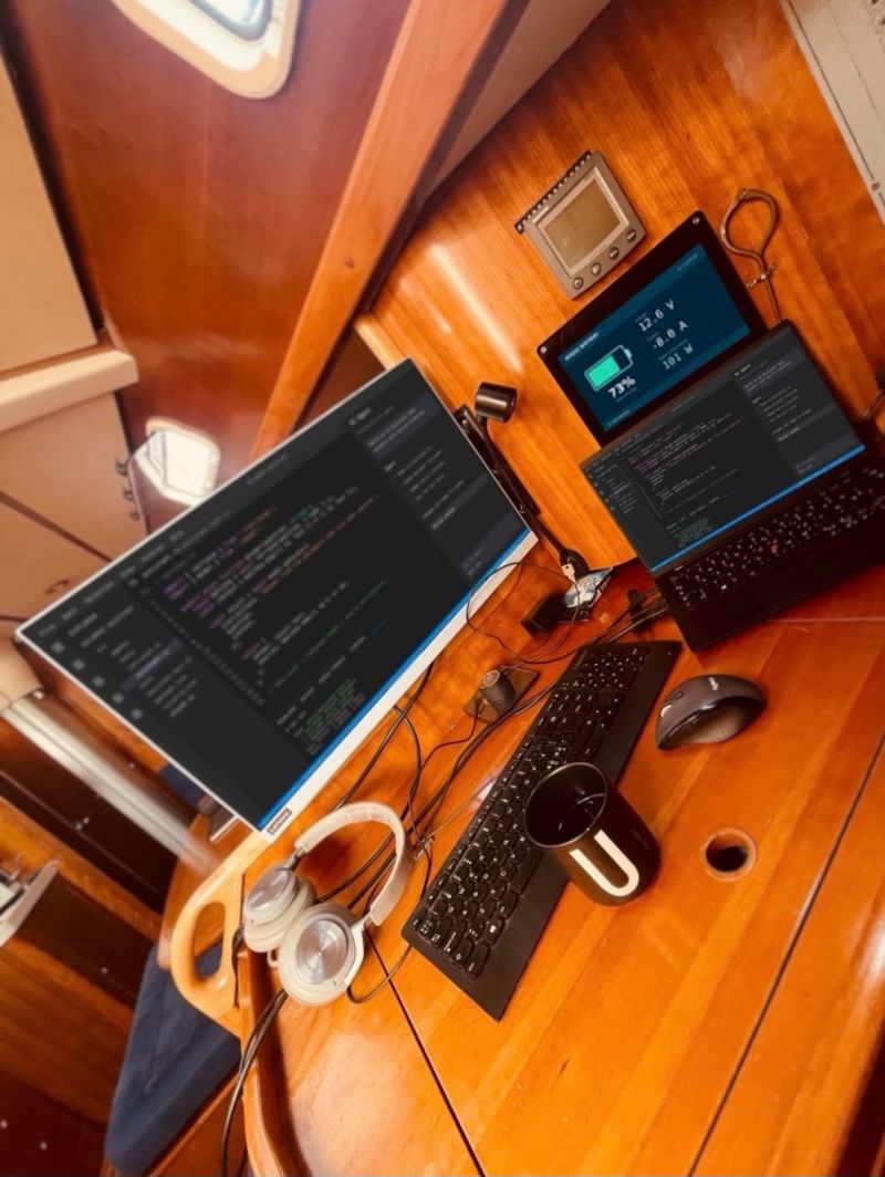 Chart table on a sailboat with a monitor, a laptop and a battery monitor showing the boat's power consumption