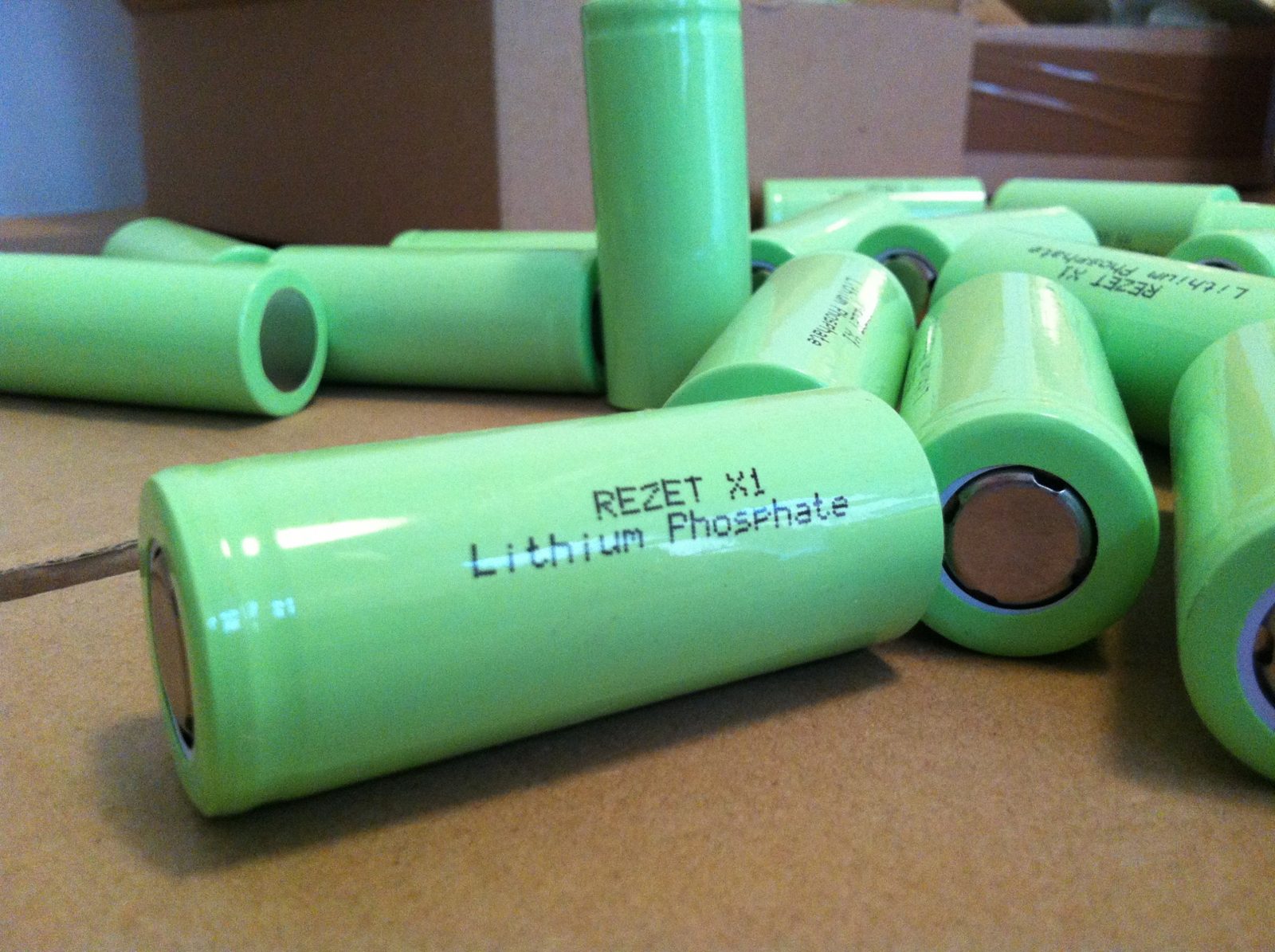 A pile of green cylindrical battery cells printed 'Rezet X1 Lithium Phosphate' on a cardboard surface