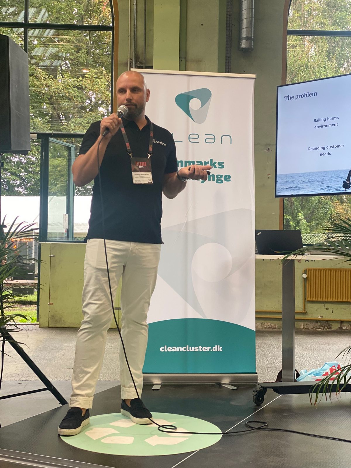 Anders on stage with a microphone, wearing an Undine shirt and a TechBBQ 2023 lanyard, next to a slide titled 'The problem'